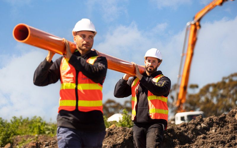 two male employees carrying a pipe